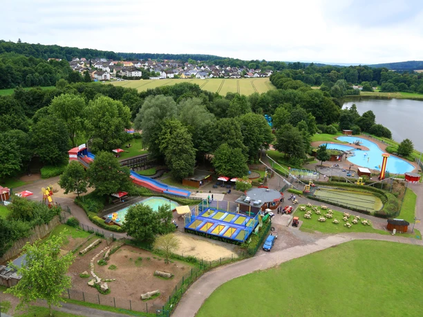 Luftaufnahme eines Freizeitparks mit Wasserrutschen, Spielplätzen, umgeben von Wald und See.