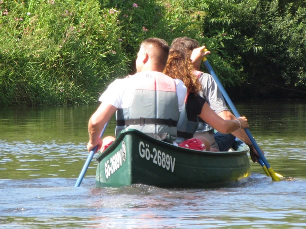 Eine dreiköpfige Gruppe paddelt bei sonnigem Wetter in grünen Westen in einem Kanu auf einem ruhigen Fluss.