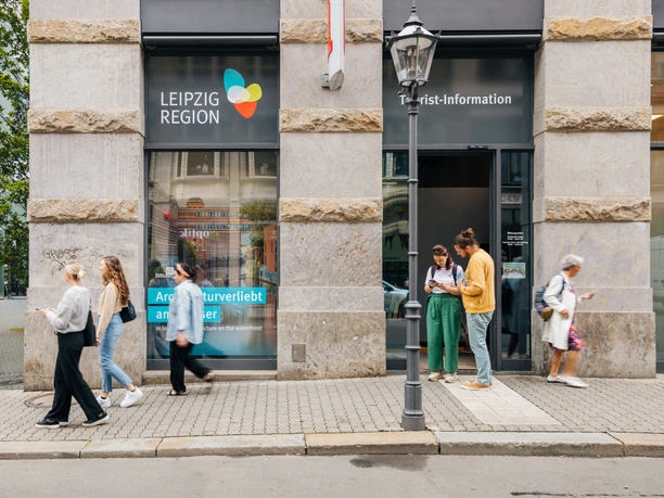 Façade et entrée principale de l'office de tourisme de Leipzig dans la Katharinenstraße 8, quelques touristes se tiennent devant l'entrée et regardent du matériel d'information.