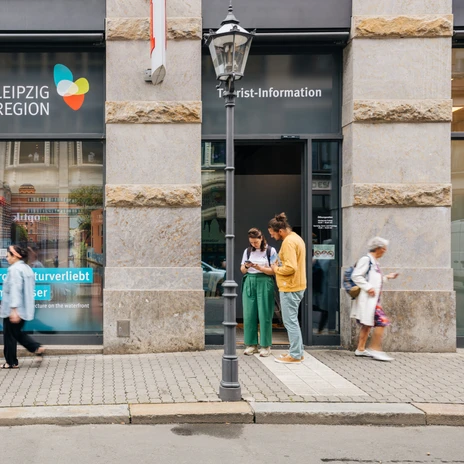 Fasada i główne wejście do Centrum Informacji Turystycznej w Lipsku przy Katharinenstraße 8, niektórzy turyści stoją przed wejściem i przeglądają materiały informacyjne