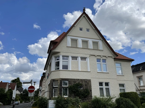 Haus Rosa mit hellem Giebel, rotem Ziegeldach und Vorgarten unter blauem Himmel