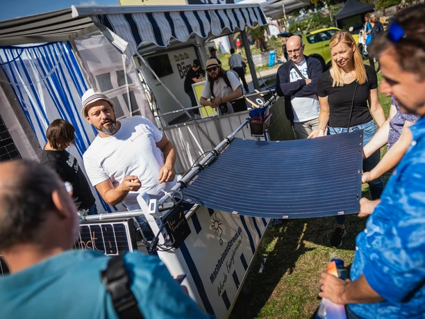 Green World Tour Cologne Five people stand at an outdoor stand and look at a flexible solar panel.