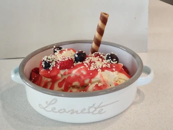 Spaghetti-Eis in weißer Schale, garniert mit Erdbeeren, Heidelbeeren und Waffelröllchen.