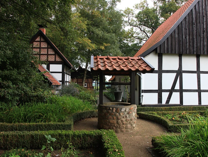 Heimatmuseum Versmold Fachwerkhäuser mit roten Ziegeldächern umgeben einen steinernen Brunnen in einem grünen Garten.