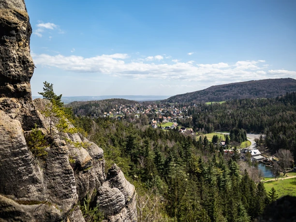 Nun rock/ Nonnenfelsen Rocks with a view of a wooded valley with houses and hills in the background.