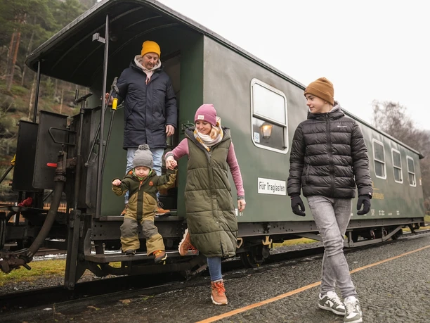 Zittauer Schmalspurbahn Eine Familie steigt fröhlich aus einem historischen Zug in einer malerischen Berglandschaft aus.