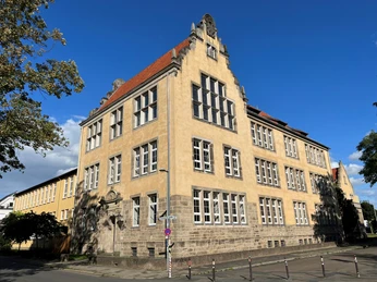 Albert Schweizer Schule Ein dreistöckiges historisches Schulgebäude mit roten Dachziegeln und zahlreichen hohen Fenstern.