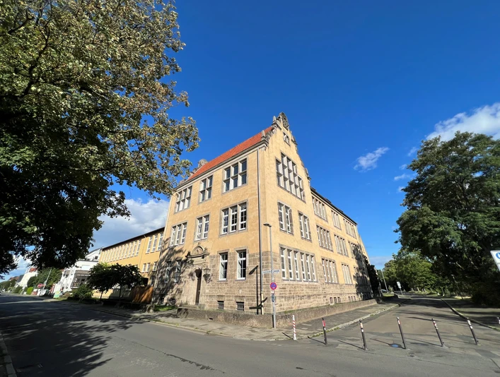 Albert Schweizer-Schule Dreistöckiges historisches Schulgebäude mit gelber Fassade und markantem Giebel unter blauem Himmel.