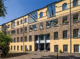 Außenansicht Kraftwerk Ermen und Engels Historisches Backsteingebäude mit gelber Fassade und modernen Glasdächern, sonniger Vorplatz.