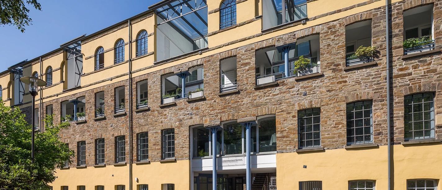 Außenansicht Kraftwerk Ermen und Engels Historisches Backsteingebäude mit gelber Fassade und modernen Glasdächern, sonniger Vorplatz.