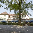 21008_Waldhotel_Baerenstein_Aussen_02.jpg Das Waldhotel Bärenstein mit umgebenden Bäumen und Terrasse mit Sonnenschirmen bei Tageslicht.