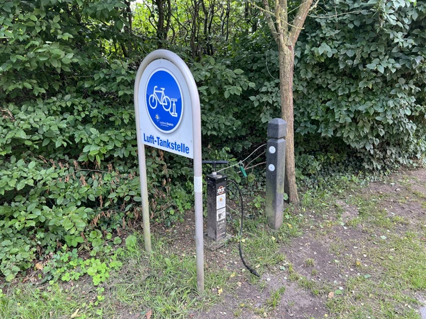 Lufttankstelle Martfeld Fahrrad-Lufttankstelle am Waldrand mit Manometer und Reifenventil, umgeben von grünem Laub.