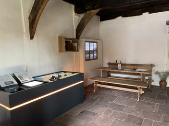 Historischer Innenraum des Pastor Hus Martfeld mit einer Holzbank, Infotafel und traditionellen Büchern.