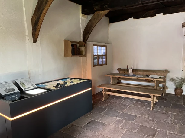 Historischer Innenraum des Pastor Hus Martfeld mit einer Holzbank, Infotafel und traditionellen Büchern.
