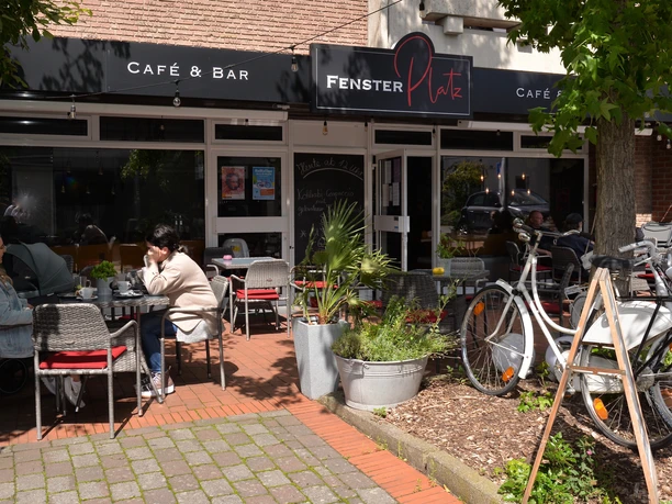 Café Fensterplatz Außensitzbereich Der Außensitzbereich des Cafés Fensterplatz bietet Tische im Freien, umgeben von Pflanzen und Fahrrädern.