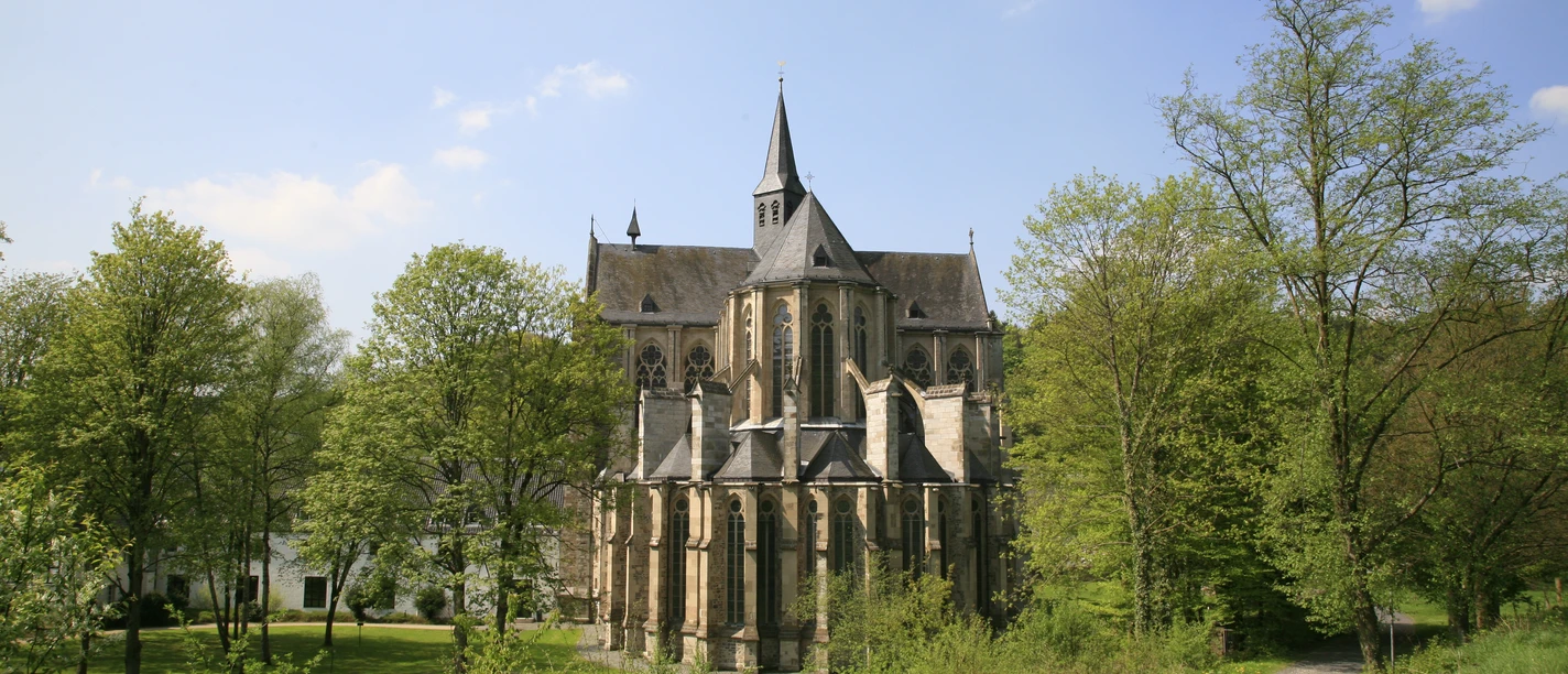 Altenberger Dom Gotische Kirche inmitten grüner Bäume bei sonnigem Wetter, gepflasterter Weg führt dorthin.