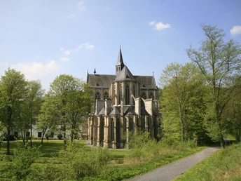Altenberger Dom Gotische Kirche inmitten grüner Bäume bei sonnigem Wetter, gepflasterter Weg führt dorthin.