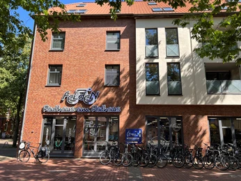 Radhaus am Rathaus Fahrradgeschäft in rotem Backsteingebäude mit breiter Glasfront, zahlreiche Fahrräder davor geparkt.