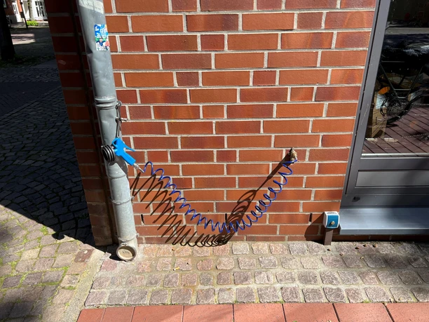 Rahaus am Rathaus Eine spiralförmige blaue Luftpumpe ist an einer roten Backsteinwand installiert, neben einem Fallrohr.