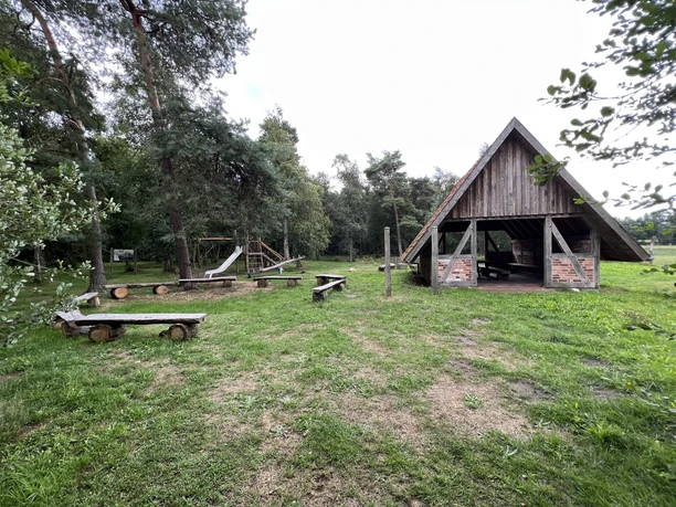 Moorkieker Offener Holz-Pavillon und Bänke auf Wiese am Waldrand, Schaukel in der Nähe, natürlicher Spielort.