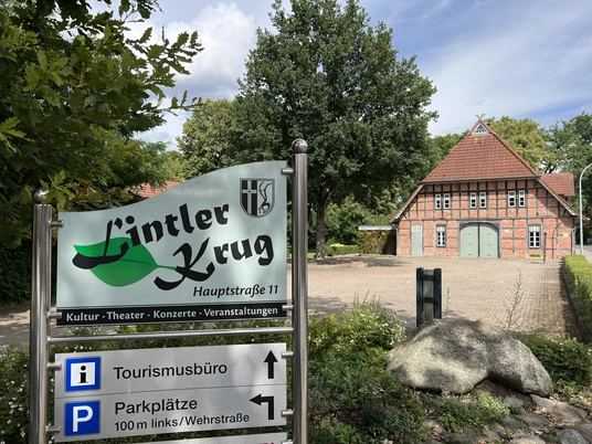 Der Lintler Krug ist ein traditionelles Backsteingebäude mit begrüntem Vorplatz und großem Baum.