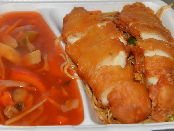 Knusprig gebackene Hähnchenbrust auf gebratenen Nudeln, neben einer pikanten Gemüse-Süß-Sauer-Sauce.