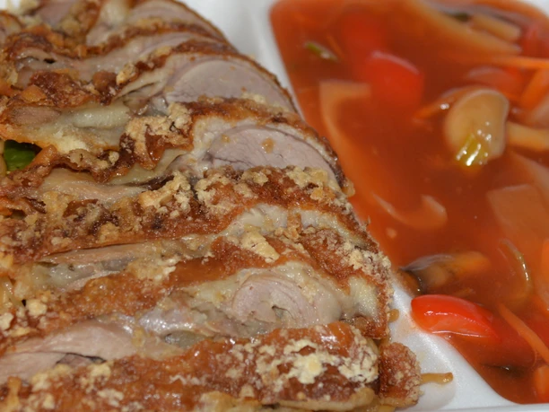 Knusprige Entenscheiben auf gebratenen Nudeln, serviert mit einer Seite würziger Gemüsesauce.