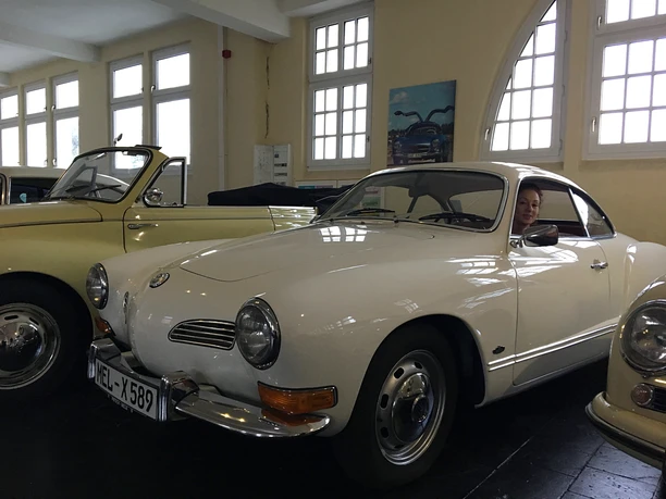 Alte Schätzchen im Automuseum Melle A woman sits smiling in a white vintage car in the Melle car museum, next to other classic cars.