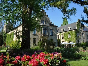 Schloss Ippenburg Schloss Ippenburg, umgeben von üppiger Vegetation und Blumen, bei sonnigem Wetter aufgenommen.