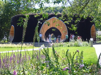 SoleArena Eine kreisförmige Holzkonstruktion umgeben von grüner Natur lädt Menschen zum Verweilen ein.A circular wooden construction surrounded by green nature invites people to linger.En cirkulær trækonstruktion omgivet af grøn natur inviterer folk til at blive hængende.Een ronde houten constructie omgeven door groene natuur nodigt mensen uit om te blijven hangen.