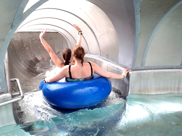 Reifenrutsche "Crazy River" Two people in a large blue tire slide through a dark spiral tunnel.