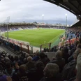 Fußballstadion bei Abendlicht mit vollen Tribünen und beleuchtetem Spielfeld, Fans jubeln lebhaft.