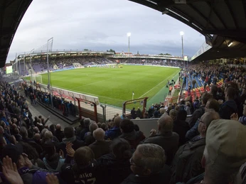 Bremer Brücke Fußballstadion bei Abendlicht mit vollen Tribünen und beleuchtetem Spielfeld, Fans jubeln lebhaft.