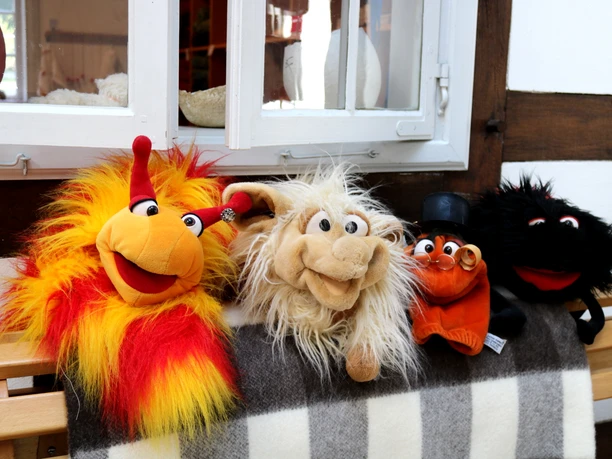 Tuchmacher Museum Bramsche im Osnabrücker Land Four colorful stuffed animals sit smiling on a wooden bench in front of a half-timbered house window.