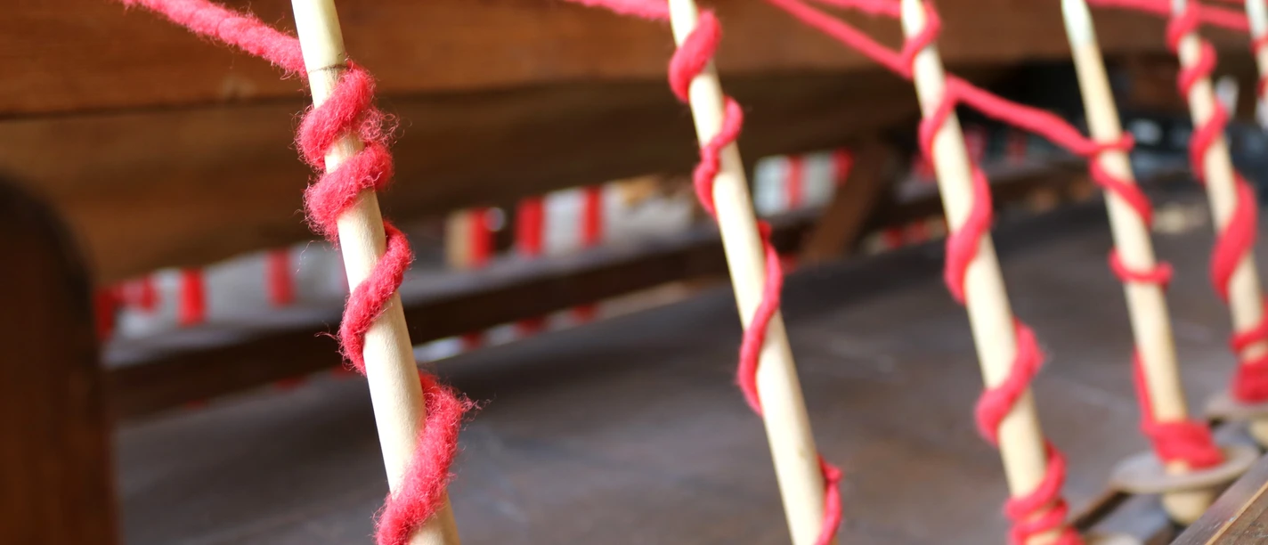 Tuchmacher Museum Bramsche im Osnabrücker Land Spindeln mit rotem Faden, bereit zur Verarbeitung in einer traditionellen Webmaschine.