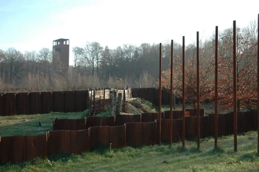 Varusschlacht im Osnabrücker Land - Museum und Park Kalkriese Historische hölzerne und metallene Grenzanlage mit Turm im Hintergrund, umgeben von Bäumen.