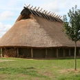 Das Eisenzeithaus in Ostercappeln-Venne Het huis van de ijzertijd in Ostercappeln-Venne is een woonstal nagebouwd uit de pre-Romeinse ijzertijd met eromheen een tuin met vergeten kruidenHistorisches Langhaus mit Reetdach auf einer Wiese, umgeben von Natur und Besuchern.