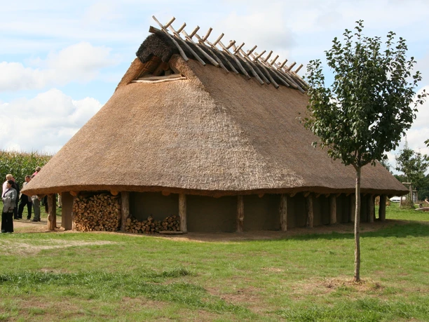 Das Eisenzeithaus in Ostercappeln-Venne Historisches Langhaus mit Reetdach auf einer Wiese, umgeben von Natur und Besuchern.