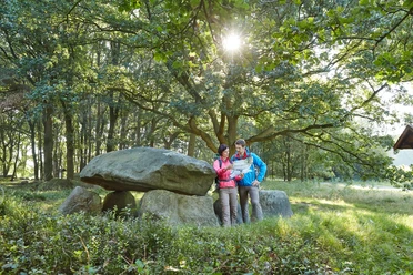 Großsteingrab Deymanns Mühle Zwei Wandernde betrachten eine Karte neben dem Großsteingrab Deymanns Mühle im lichten Wald.