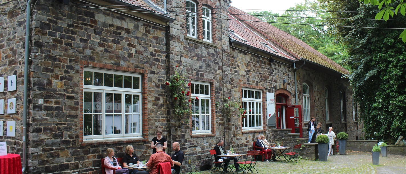 Das Piesberger Gesellschaftshaus in Osnabrück Historisches Backsteingebäude mit roten Tischen und Stühlen im Freien, umgeben von grüner Natur.