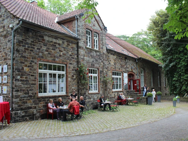 Das Piesberger Gesellschaftshaus in Osnabrück Historisches Backsteingebäude mit roten Tischen und Stühlen im Freien, umgeben von grüner Natur.