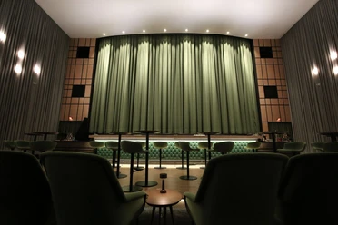 Capitol Theater Kinosaal mit grünem Vorhang auf der Bühne und Barhockern im Vordergrund.