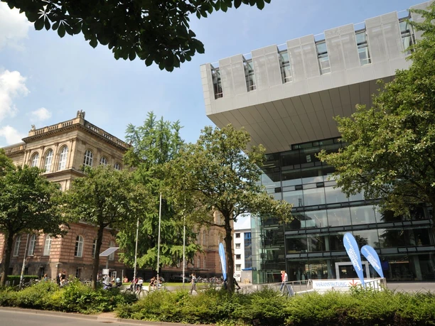 SuperC Modernes Gebäude in C-Form mit Glasfront und einem Vorplatz, umgeben von grünen Bäumen. Links daneben steht ein Gebäude mit historischer Fassade.