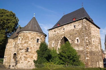 Ponttor Historisches Stadttor mit zwei Türmen aus Naturstein und mehreren Bäumen davor.