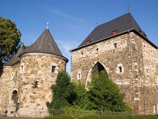 Ponttor Historisches Stadttor mit zwei Türmen aus Naturstein und mehreren Bäumen davor.