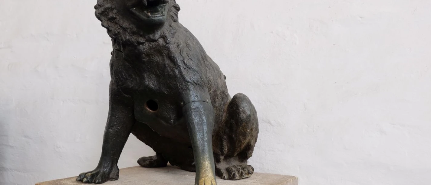 Wolfsskulptur mit aufgerissenem Maul sitzt auf einem Sockel.