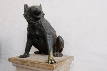 Wolf Wolfsskulptur mit aufgerissenem Maul sitzt auf einem Sockel.