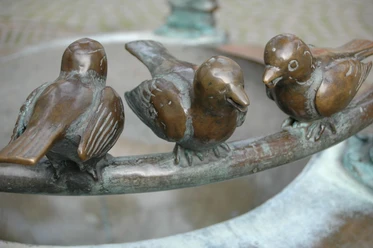 Möschebrunnen Drei Spatzen aus Bronze sitzen auf dem Rand eines Brunnens.