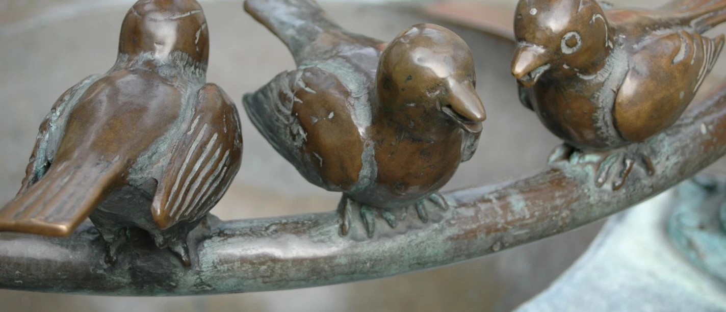 Möschebrunnen Drei Spatzen aus Bronze sitzen auf dem Rand eines Brunnens.