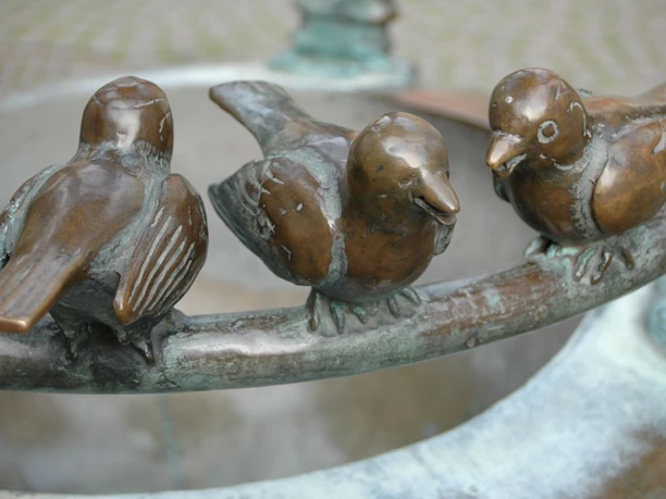 Möschebrunnen Drei Spatzen aus Bronze sitzen auf dem Rand eines Brunnens.